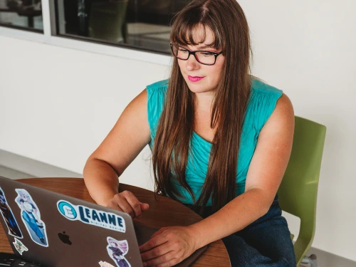 Designer sitting at a table working on a laptop covered in stickers while reviewing a Winnipeg logo design project.